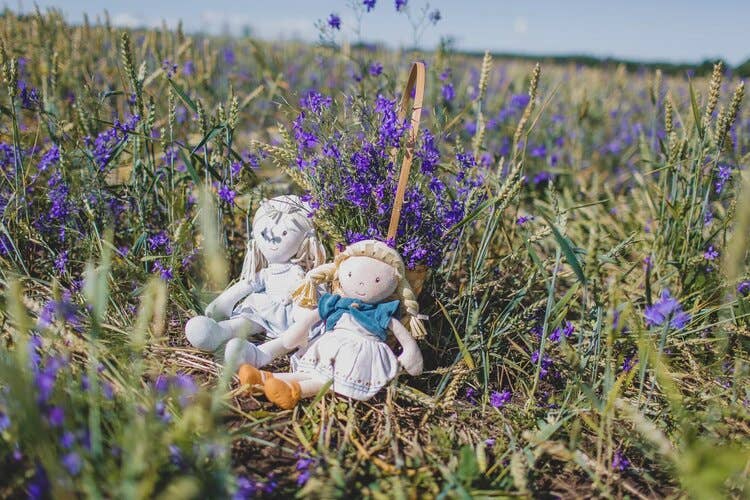Two dolls in a basket surrounded by purple flowers in a field