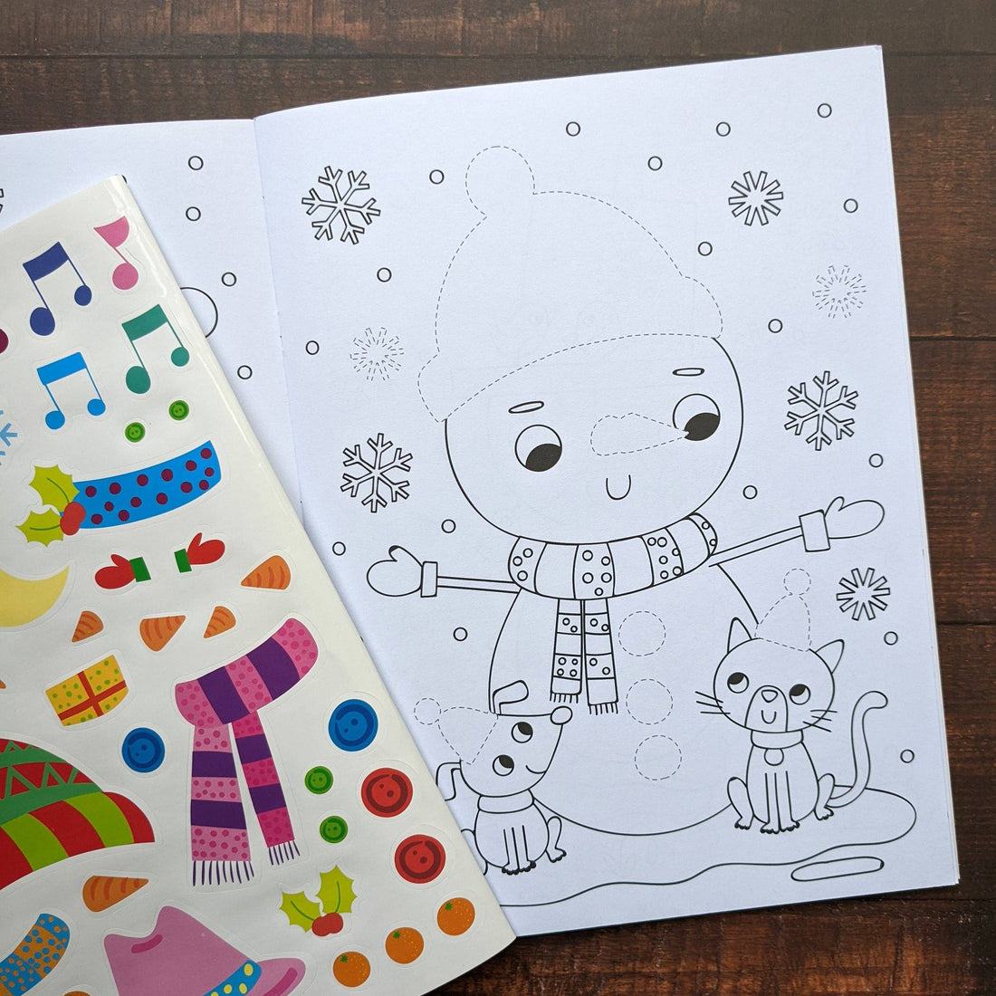 Children's activity book titled 'Dress Me Up Snowman' with a snowman and elf illustration on a wooden surface.