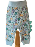 Joggers covered in brightly colour dinosaurs and scales coming out of one leg on a white background.