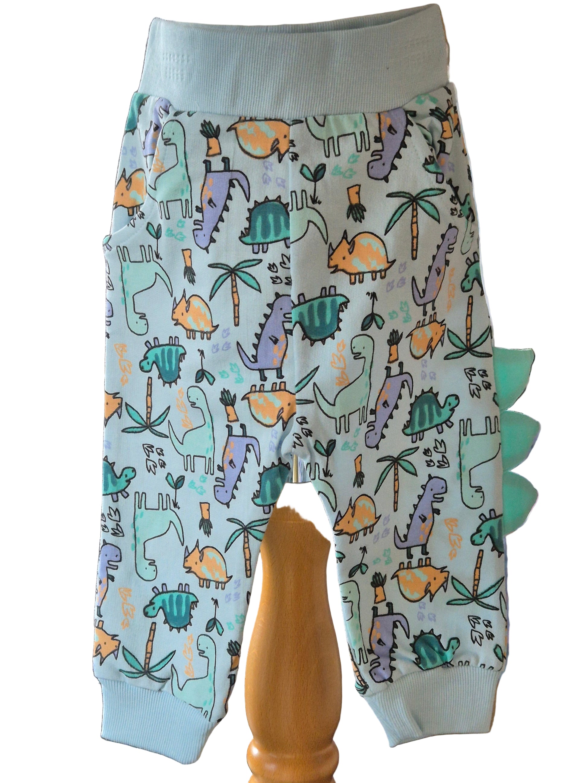 Joggers covered in brightly colour dinosaurs and scales coming out of one leg on a white background.