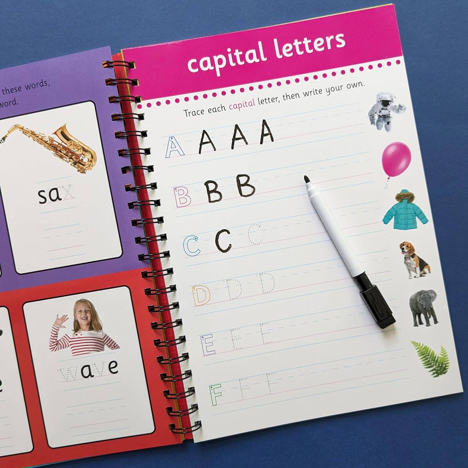 Open educational book with alphabet tracing pages and a pen on a blue background