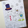 Coloring book page with a snowman and reindeer illustration on a wooden surface.