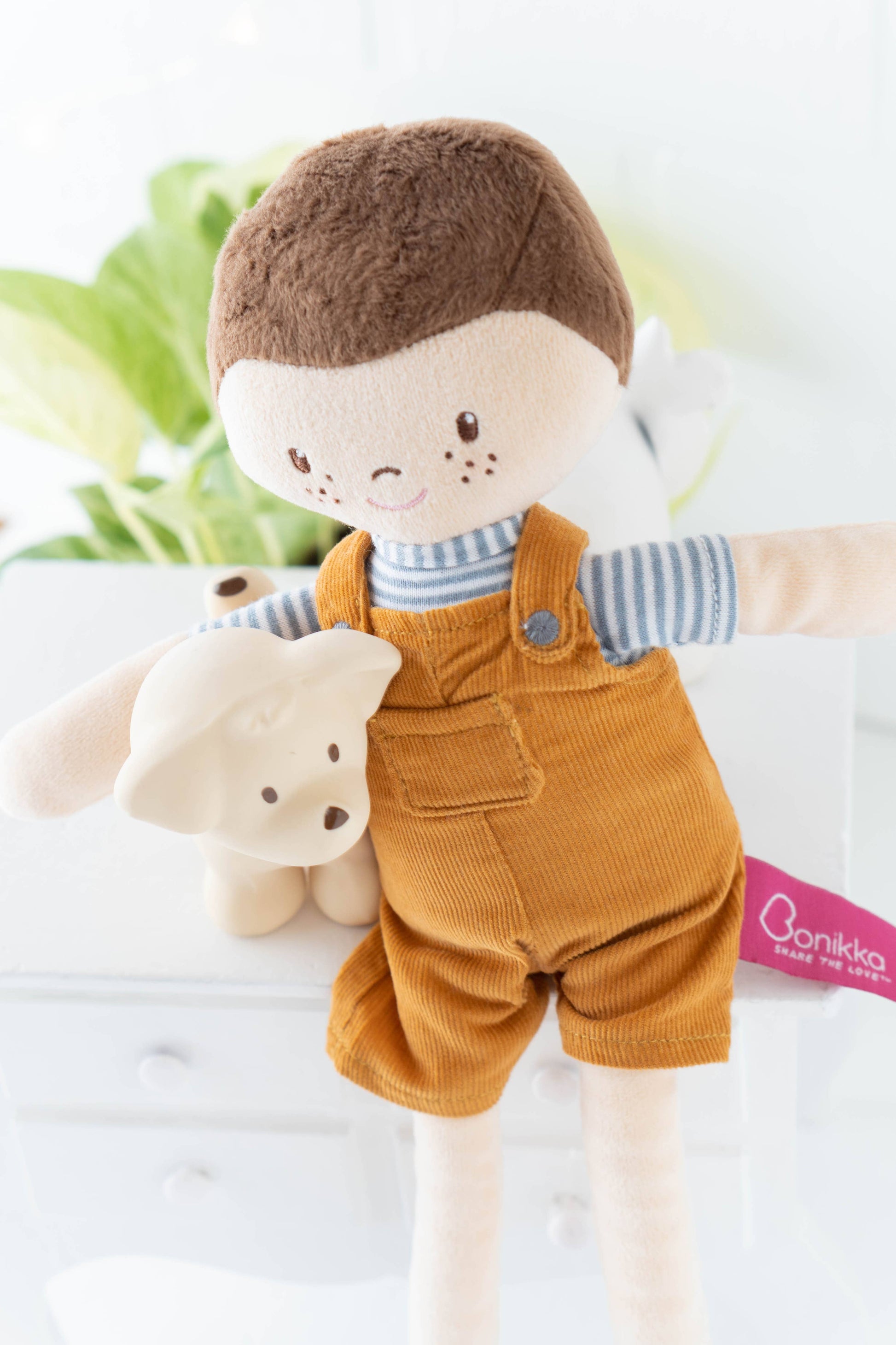 Doll wearing mustard yellow overalls holding a teddy bear with a blurred background