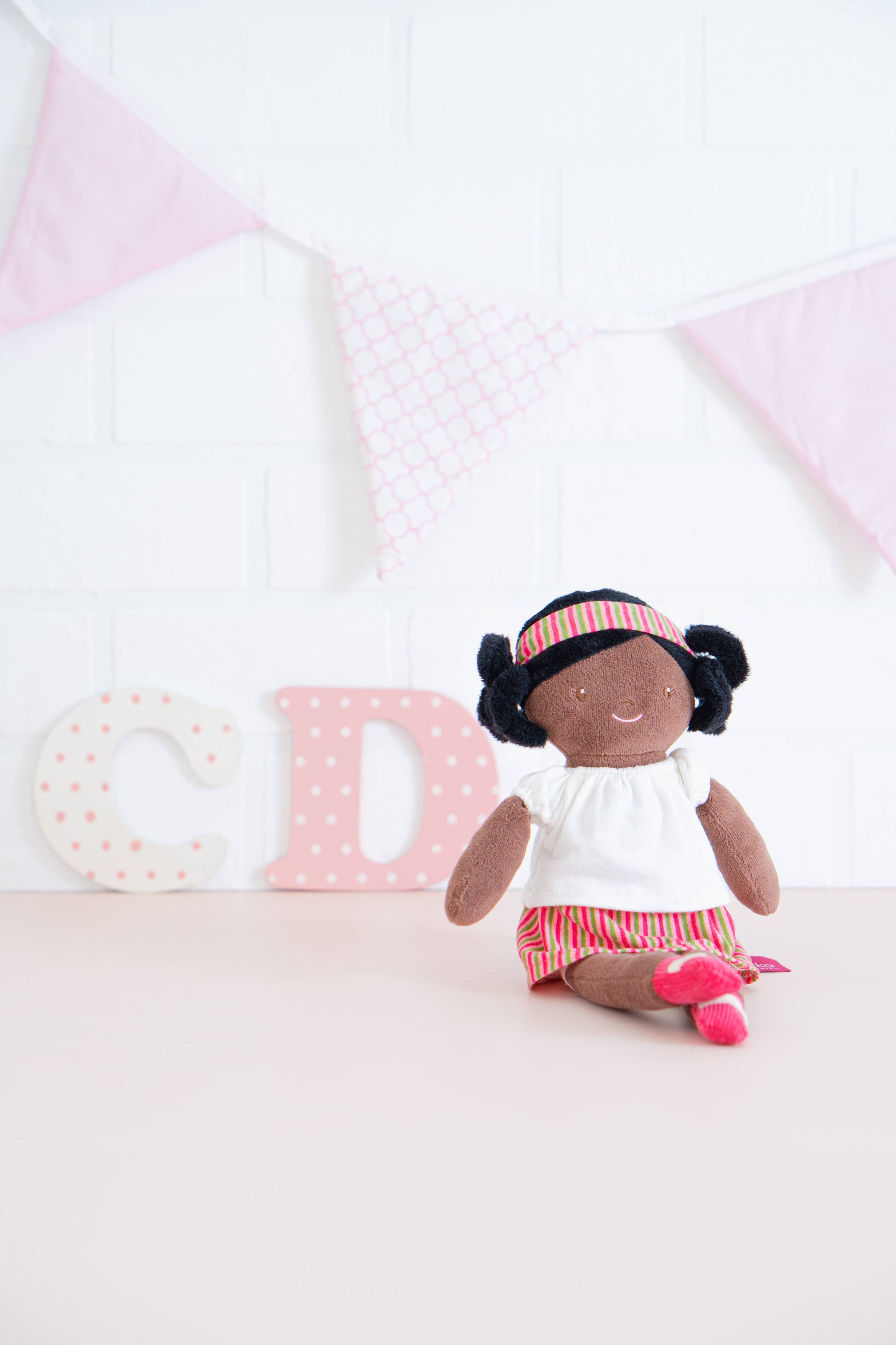 Small doll with black hair wearing a white dress and red headband on a light background