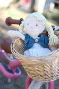 Doll with blonde hair and blue dress in a wicker basket on a pink bicycle