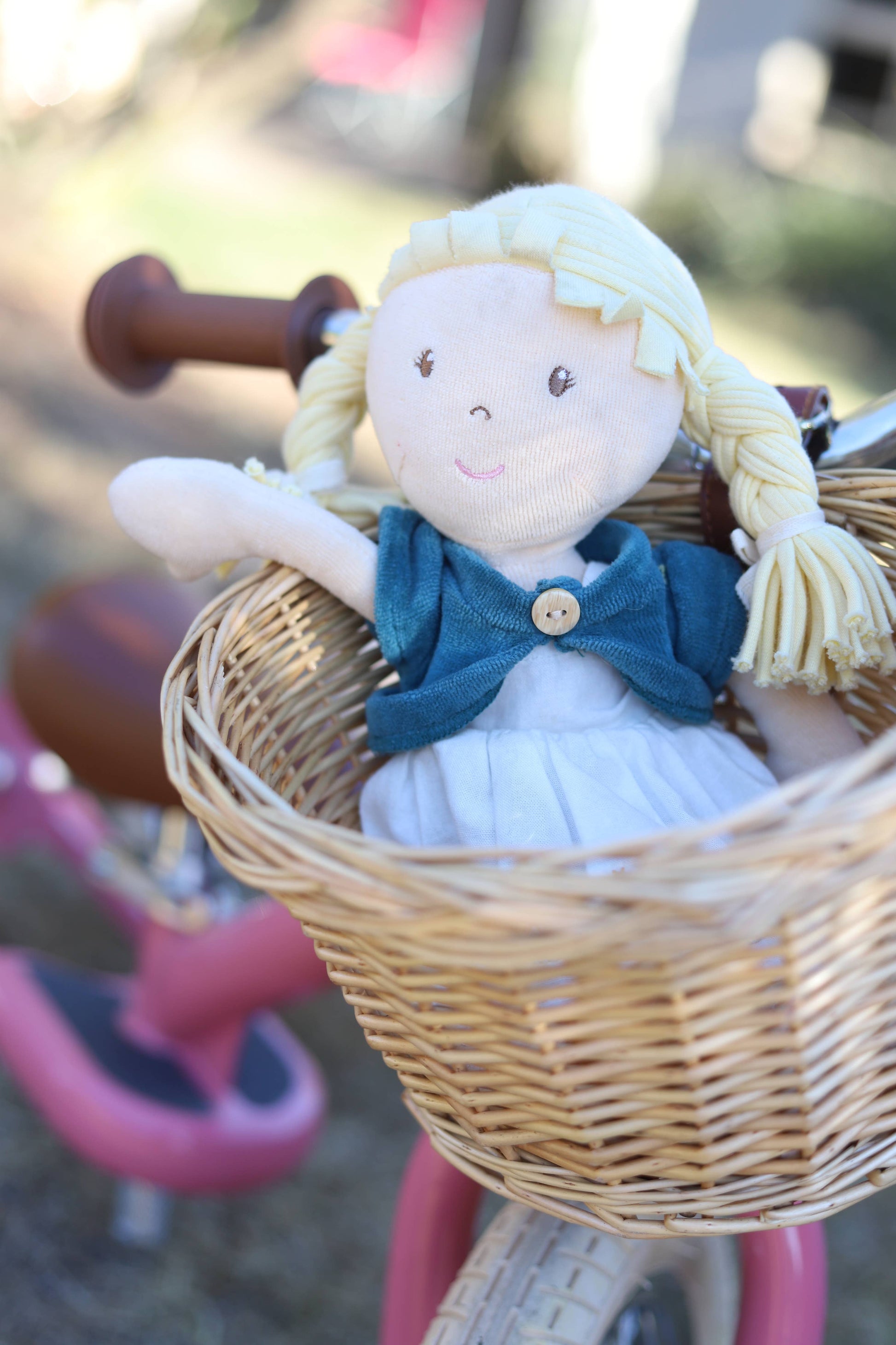 Doll with blonde hair and blue dress in a wicker basket on a pink bicycle