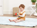 Child playing with a toy on a light blue rug in a room with white walls and wooden flooring.