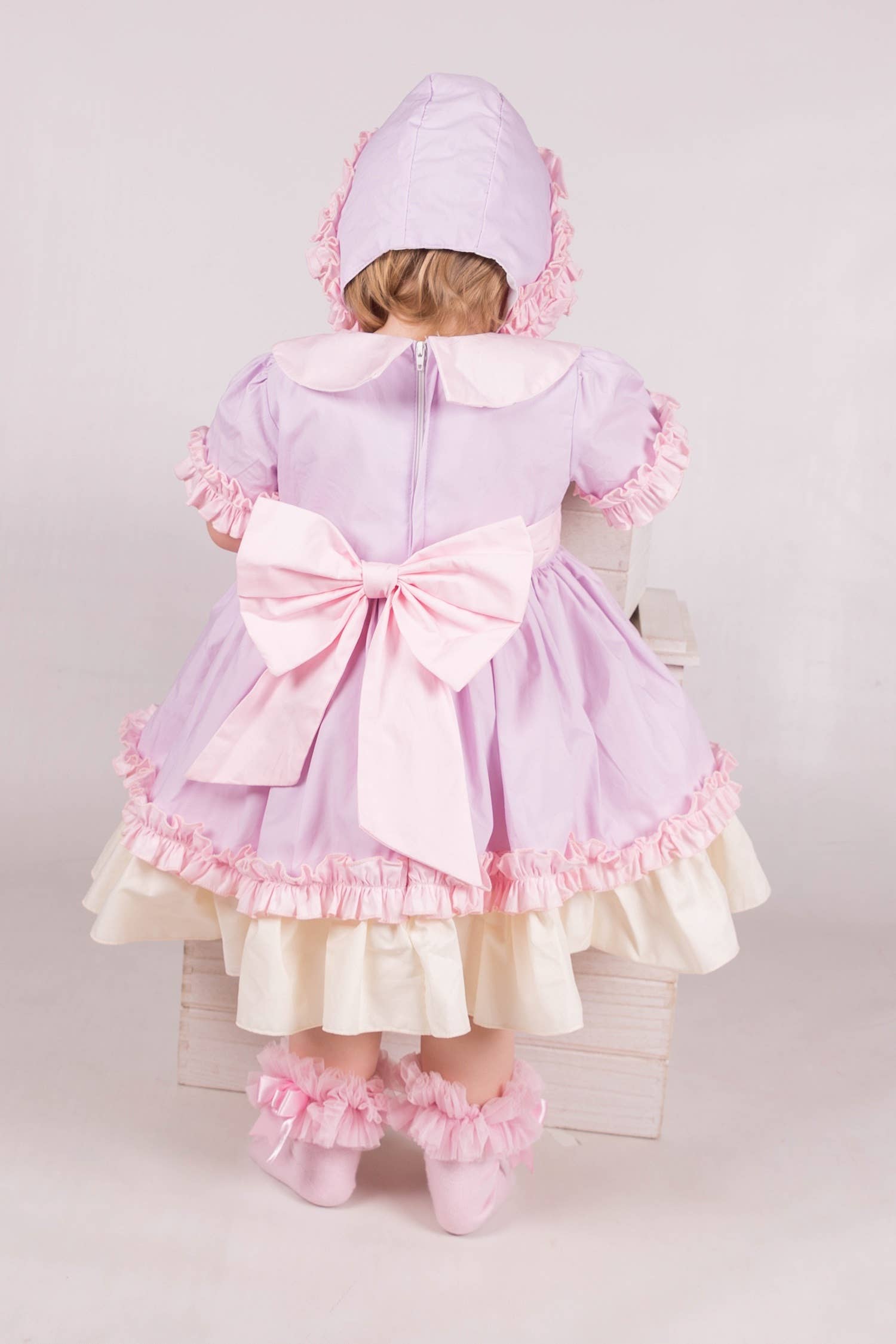 Child wearing a pink and purple dress with a large bow on a white background