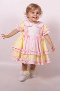Child wearing a pink and yellow dress with ruffles on a plain background