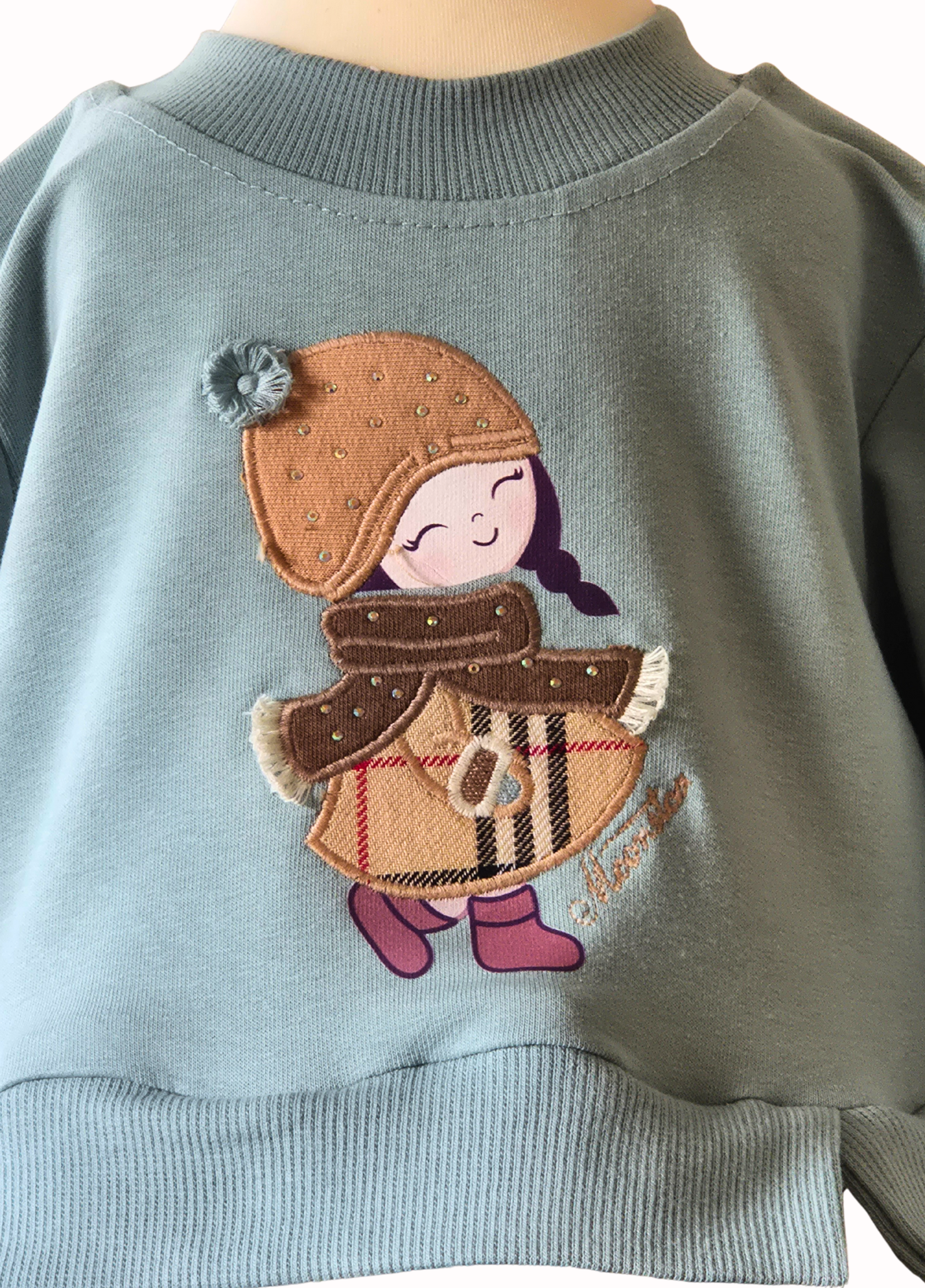Sweatshirt with a embroidered design of a child wearing a hat, scarf, and coat on a light blue background.