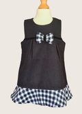 Black sleeveless dress with a plaid bow and hem on a mannequin against a beige background