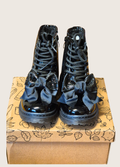 Pait of black patent boots with shiny bows sat on a shoe box
