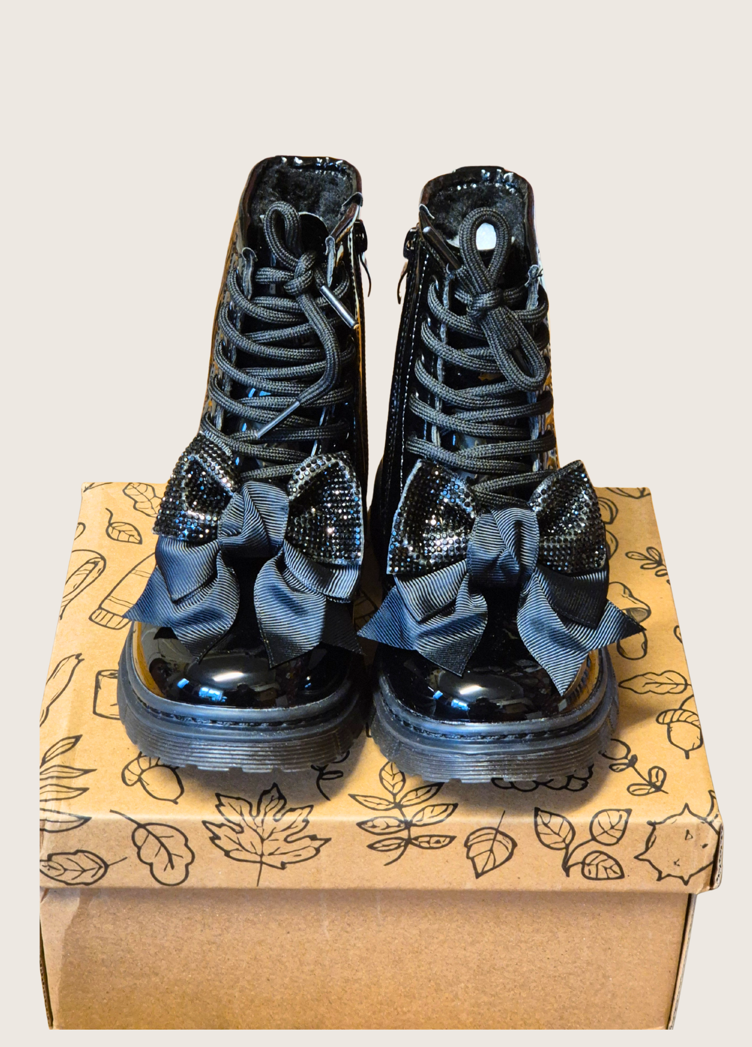 Pait of black patent boots with shiny bows sat on a shoe box
