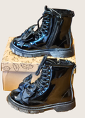 Side view of a pair of black patent boots with shiny bows one on a show box one below