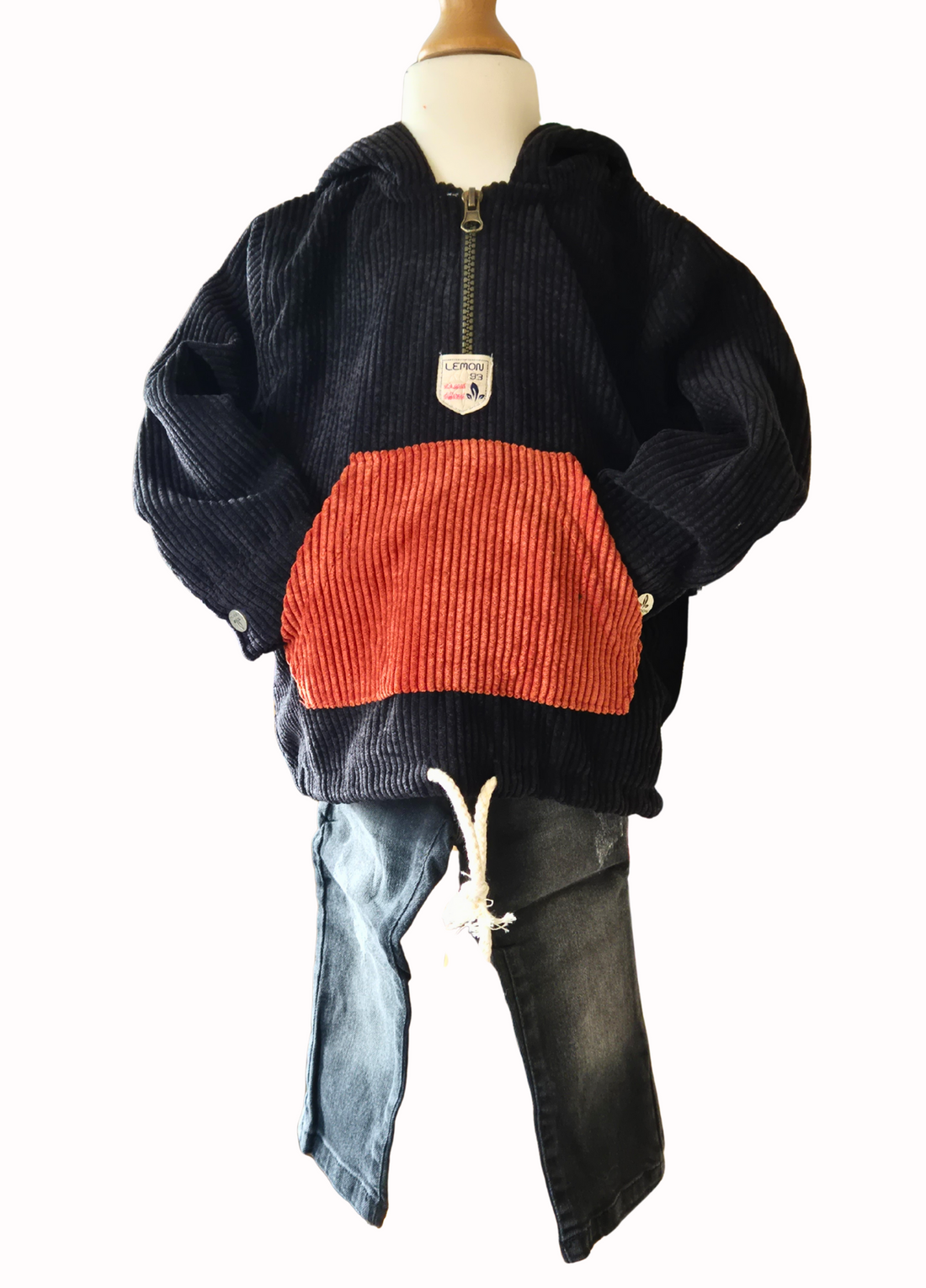Black distressed jeans and a black and rust cord hoodie on a mannequin against a white background