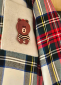 Plaid shirt with a cartoon bear pin on a textured surface