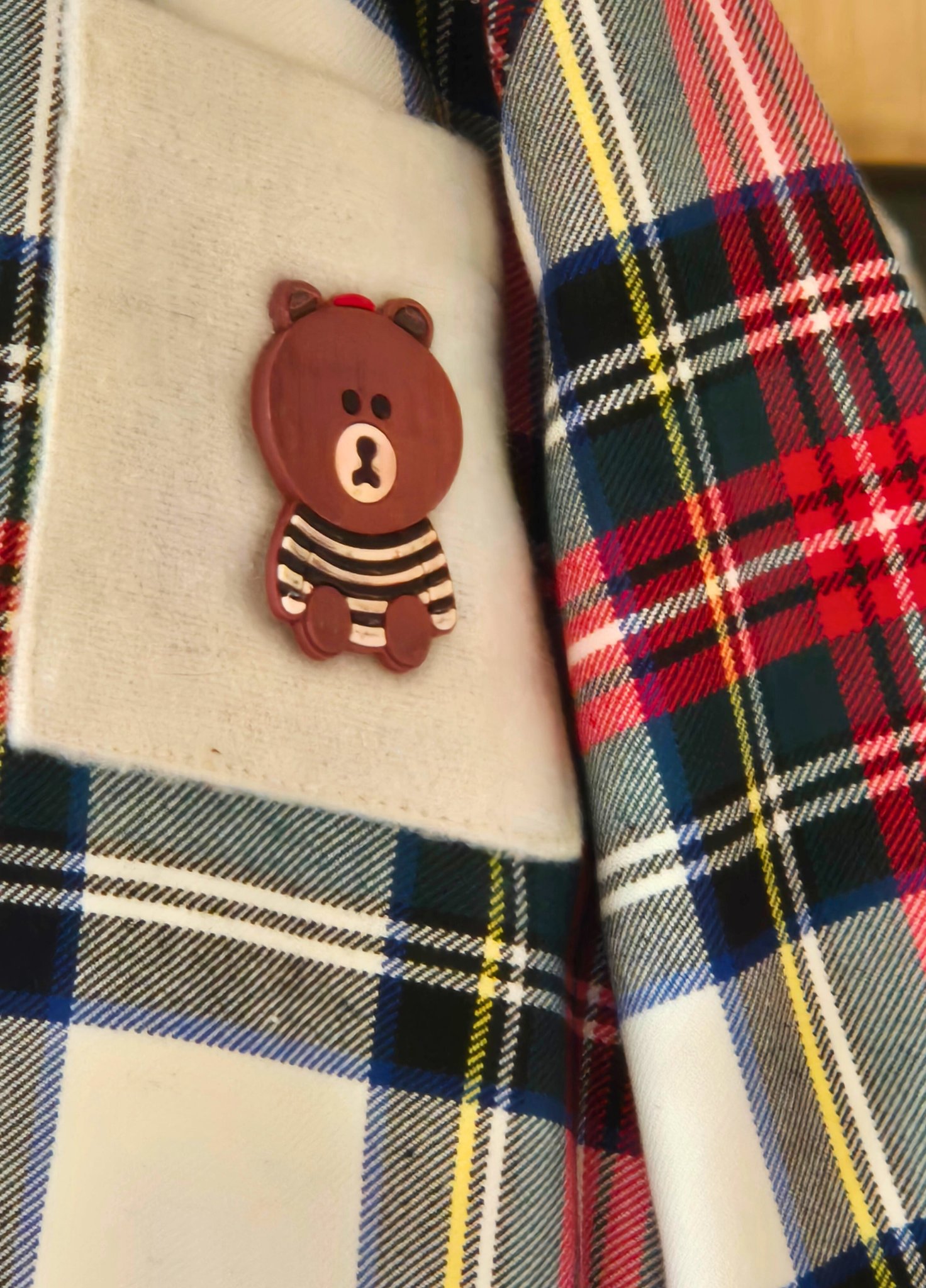 Plaid shirt with a cartoon bear pin on a textured surface