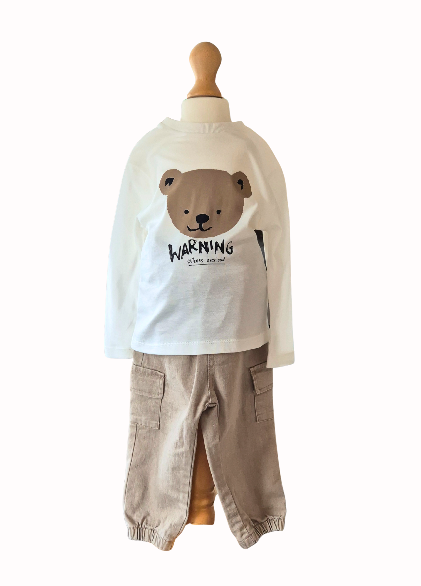 Children's outfit with a white shirt featuring a bear design and beige pants on a mannequin against a white background.