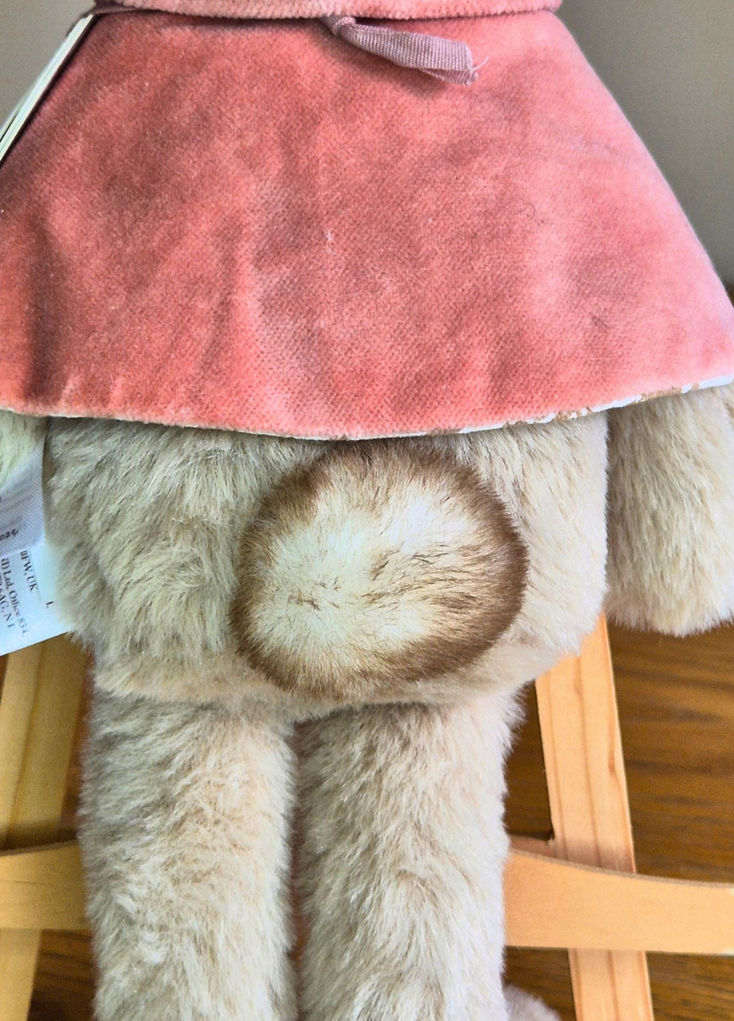 Close-up of Flopsy Rabbit plush toys tail wearing a pinkcape on a wooden surface