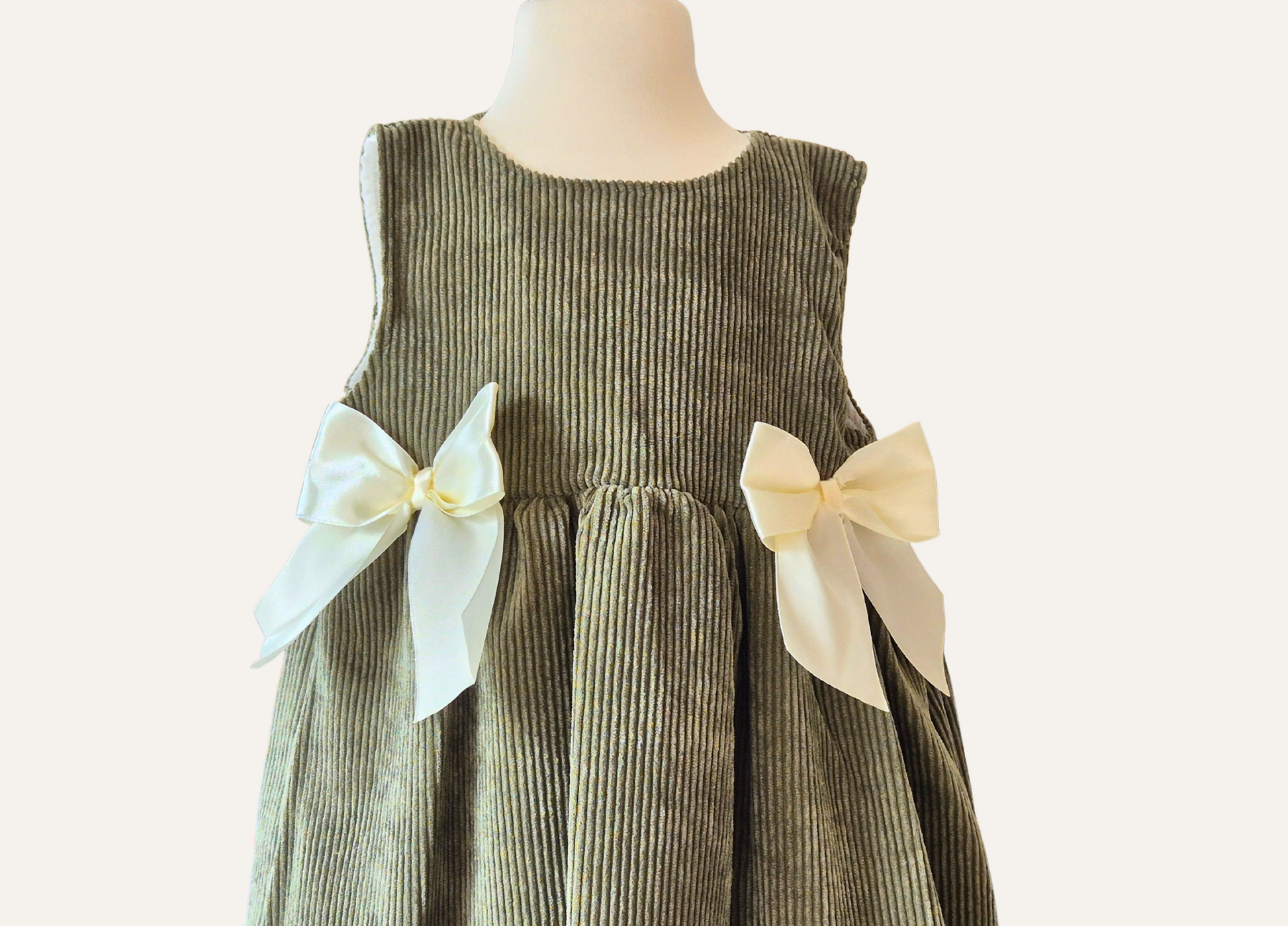 Close up detail of girls Spanish olive green pinafore dress with cream bows