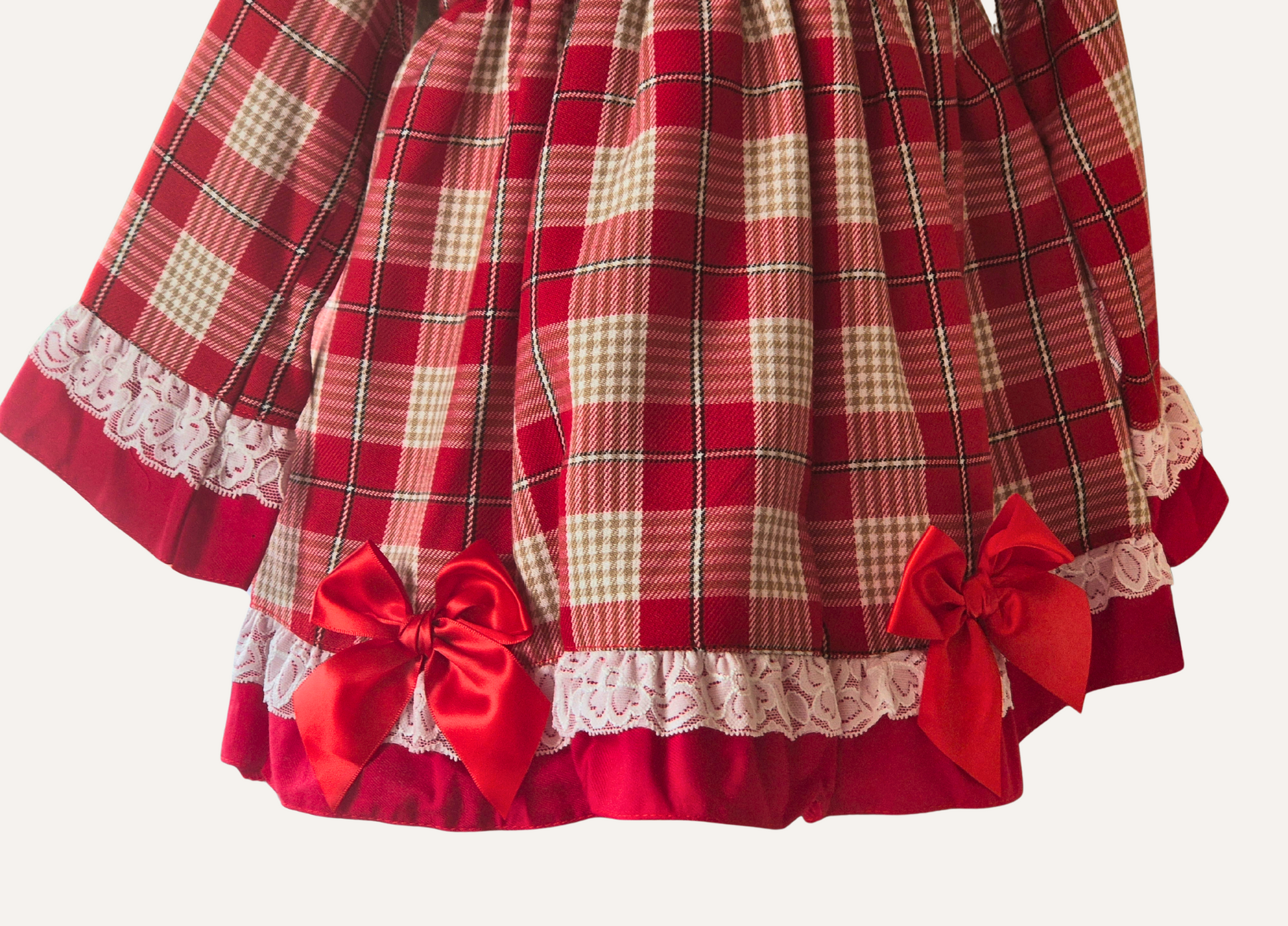 Close up of the hemline on girls Spanishred plaid dress with lace and red bows.
