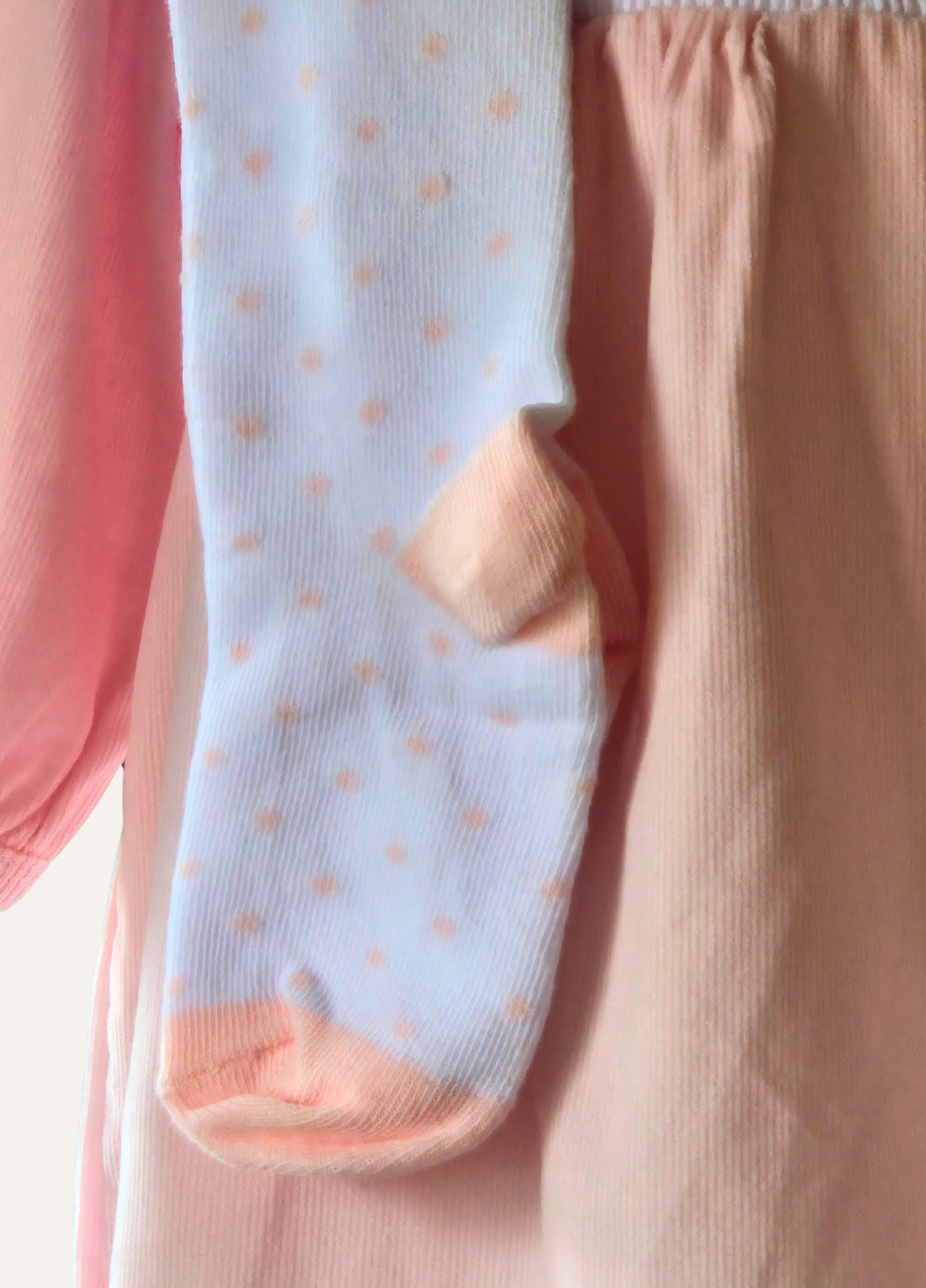 Close up of white tights with pink polka dots part of the 3 piece  girls pink smocked dress set