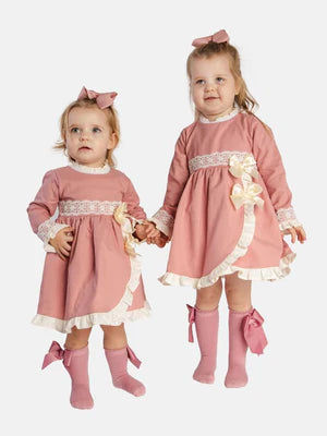 Two young girls wearing matching dusky pink spanish dresses with lace details and double bows