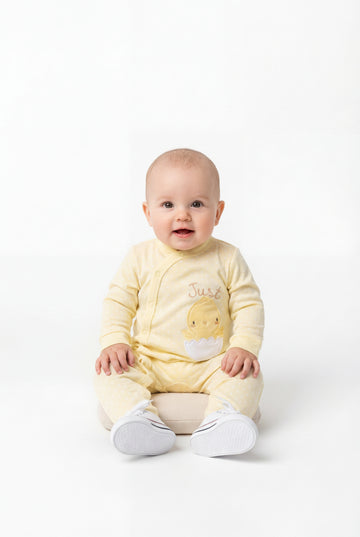 Baby wearing a yellow onesie with a cartoon design on a white background