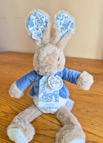 Stuffed licensed Peter Rabbit toy with blue floral ears and outfit on a wooden surface