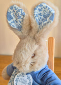 Stuffed toy rabbit with floral ears and a 'Peter Rabbit' tag on a wooden surface.