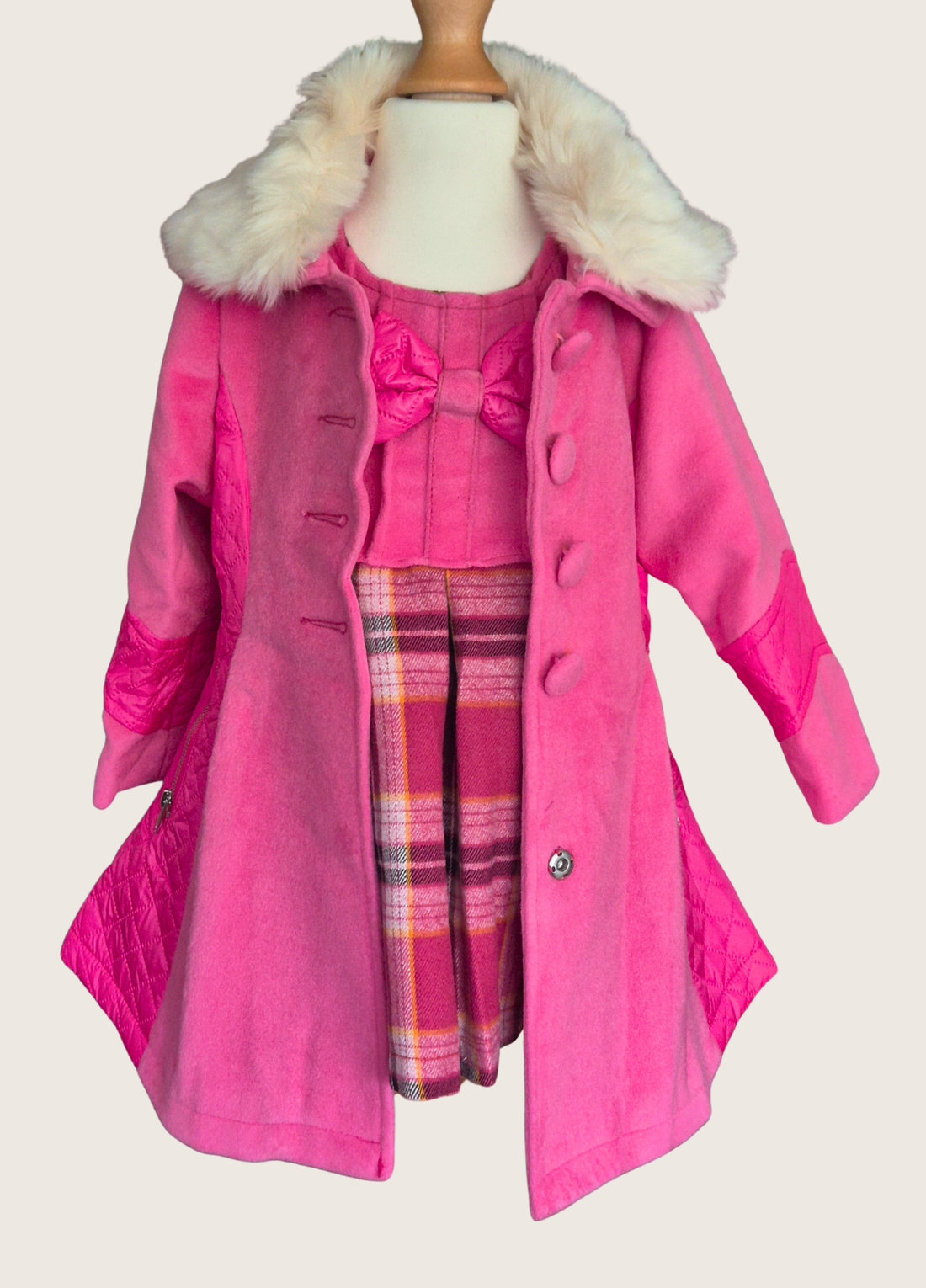 Child wearing a pink coat with white fur trim in front of a floral wall.