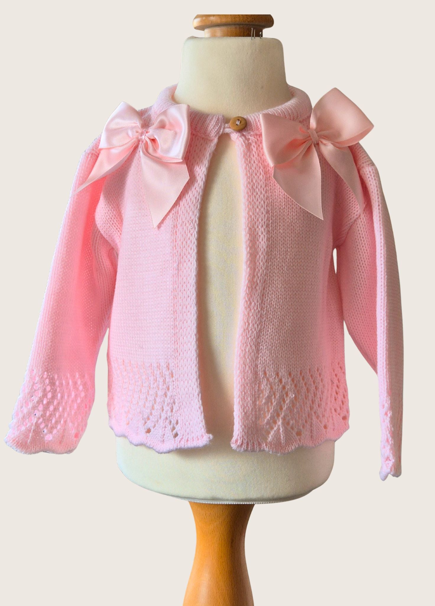 Pink knitted cardigan with bow details on a mannequin against a white background