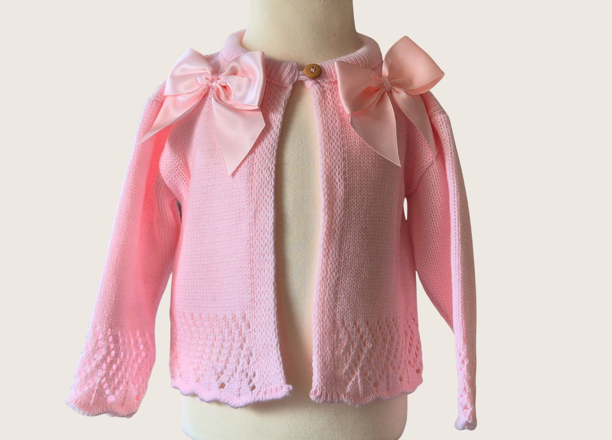 Pink knitted cardigan with bow details on a mannequin against a light background