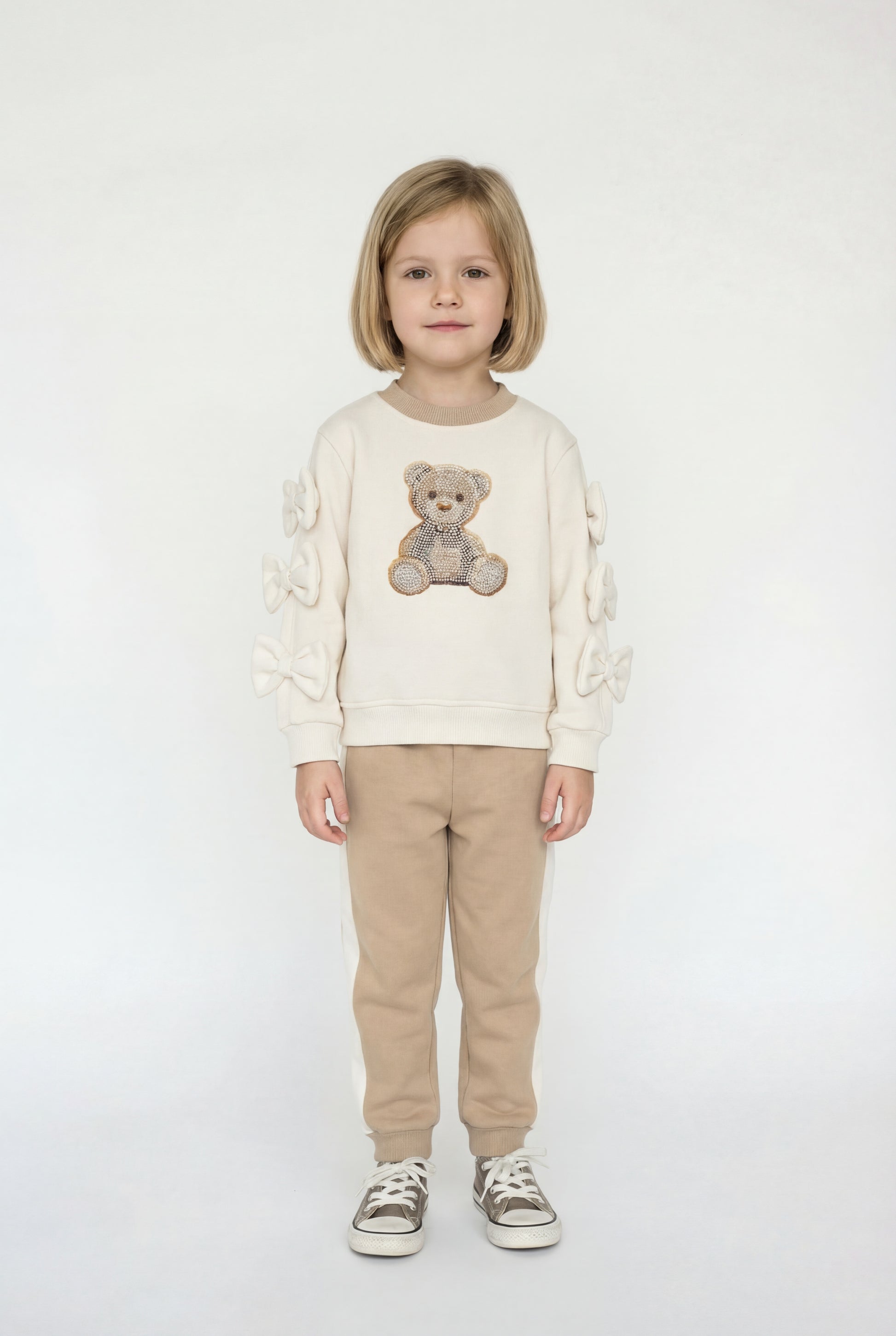Child wearing a cream sweater with a teddy bear design and beige pants on a white background