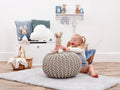 Child playing with Flopsy Rabbit  on a pouf in a room with decorative items.
