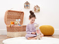 Child playing with stuffed animals next to a wicker basket filled with toys on a wooden floor.