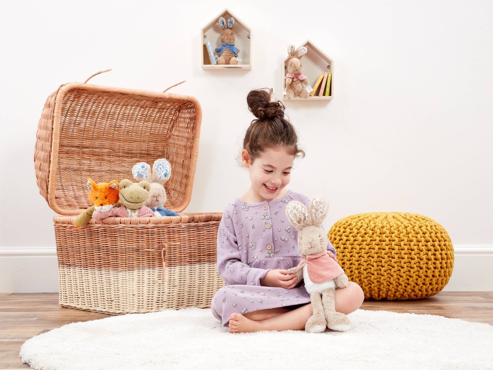Child playing with stuffed animals next to a wicker basket filled with toys on a wooden floor.
