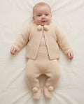 Soft beige knitted newborn baby cardigan and footed trousers set with matching pom pom details