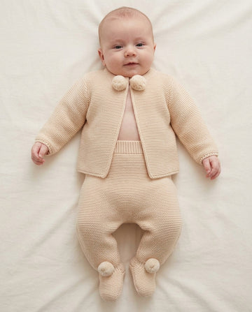 Soft beige knitted newborn baby cardigan and footed trousers set with matching pom pom details