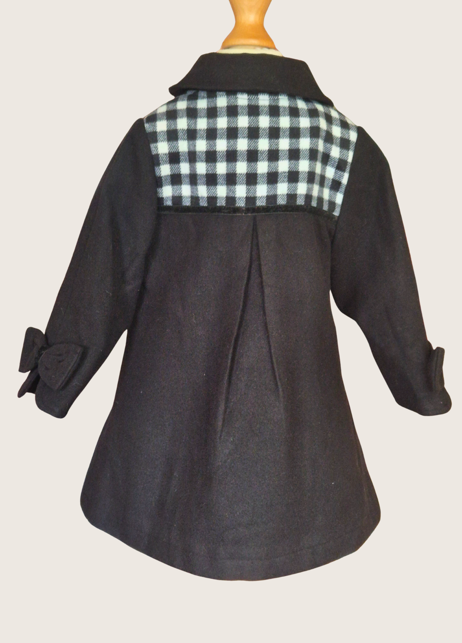 Back view of black coat with checkered pattern on a mannequin against a beige background