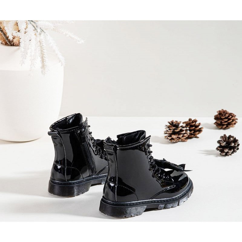 Back view of a pait of shiny black patent boots styled on a white background with pinecones and a white vase.