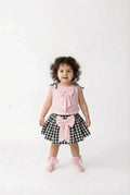 Child wearing a pink top and black and white checkered skirt with a bow on a white background