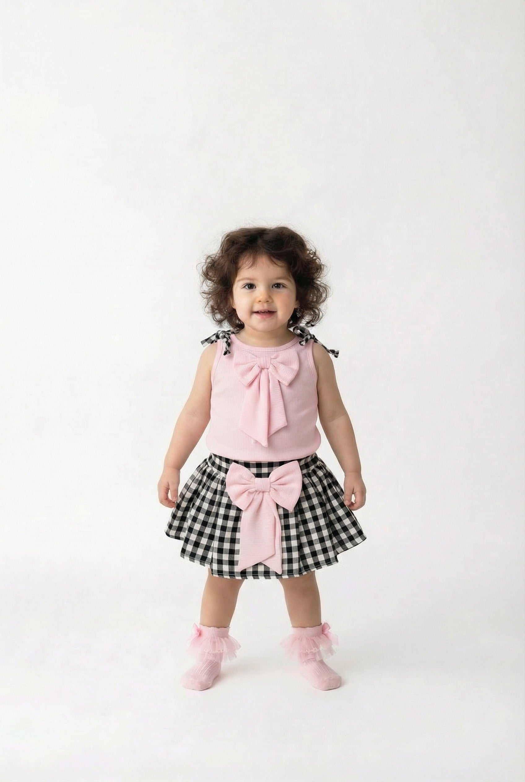 Child wearing a pink top and black and white checkered skirt with a bow on a white background