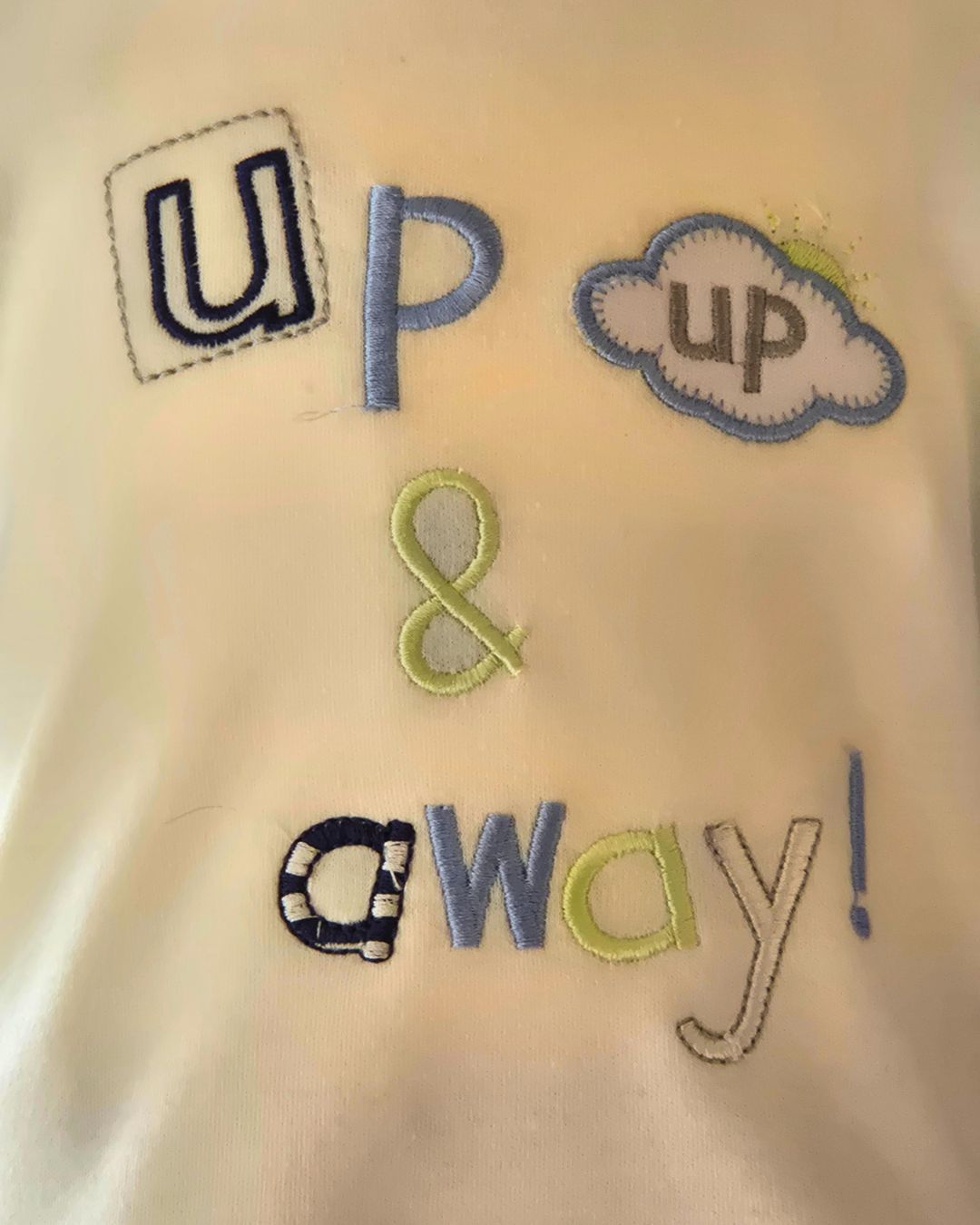 Embroidered text 'up & away!' on a fabric background