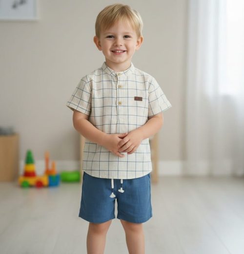 Young boy wearing a checkered shirt and blue shorts indoors.