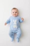 Baby in a blue knitted romper with a white rabbit on the front on a pale background.
