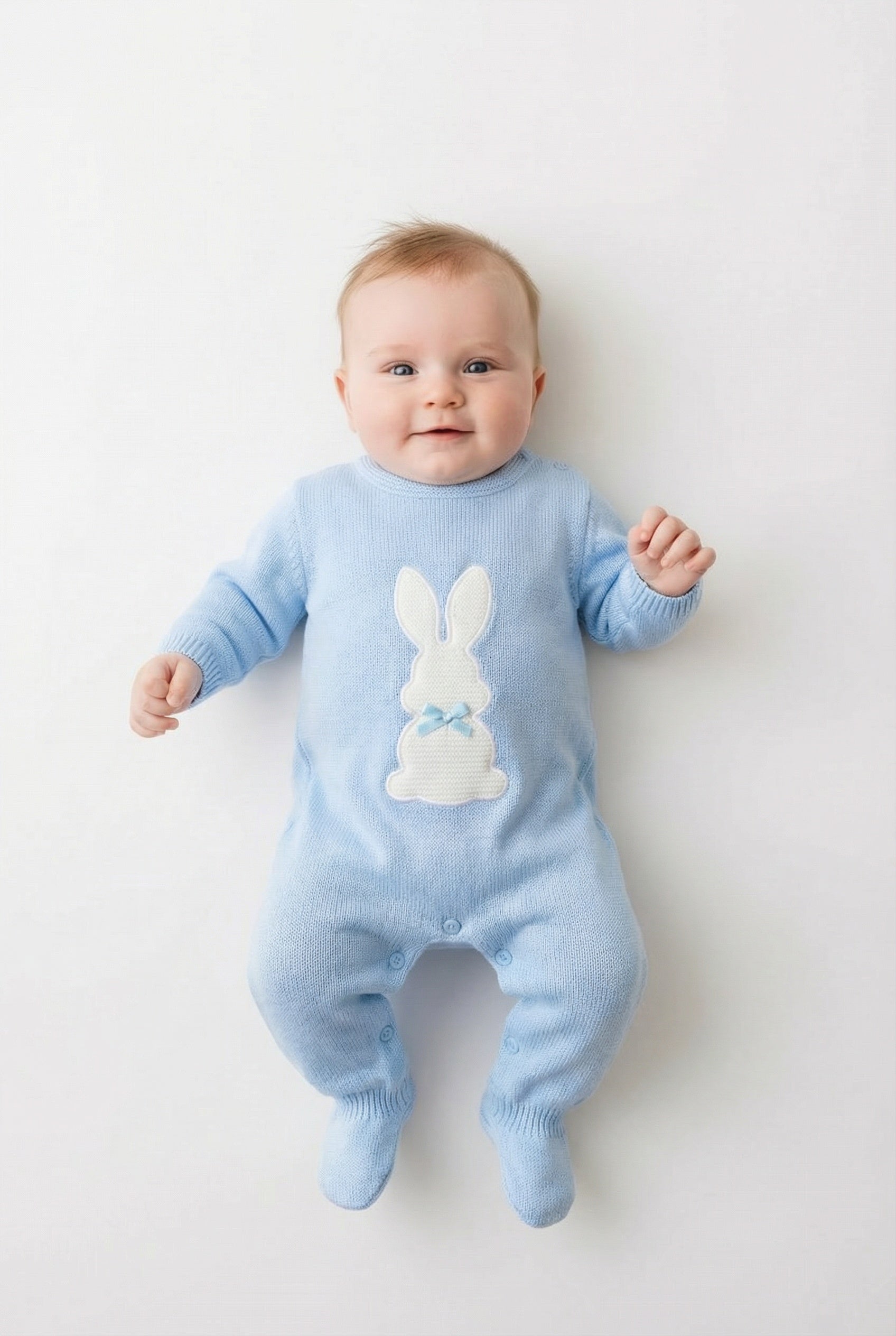 Baby in a blue knitted romper with a white rabbit on the front on a pale background.