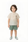 Child wearing a checkered shirt and green shorts on a white background