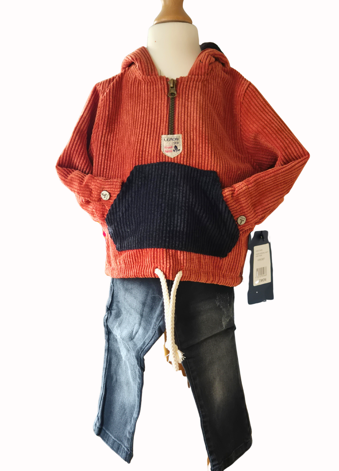 Children's outfit with orange corduroy hoodie, black jeans, on a mannequin against a white background.