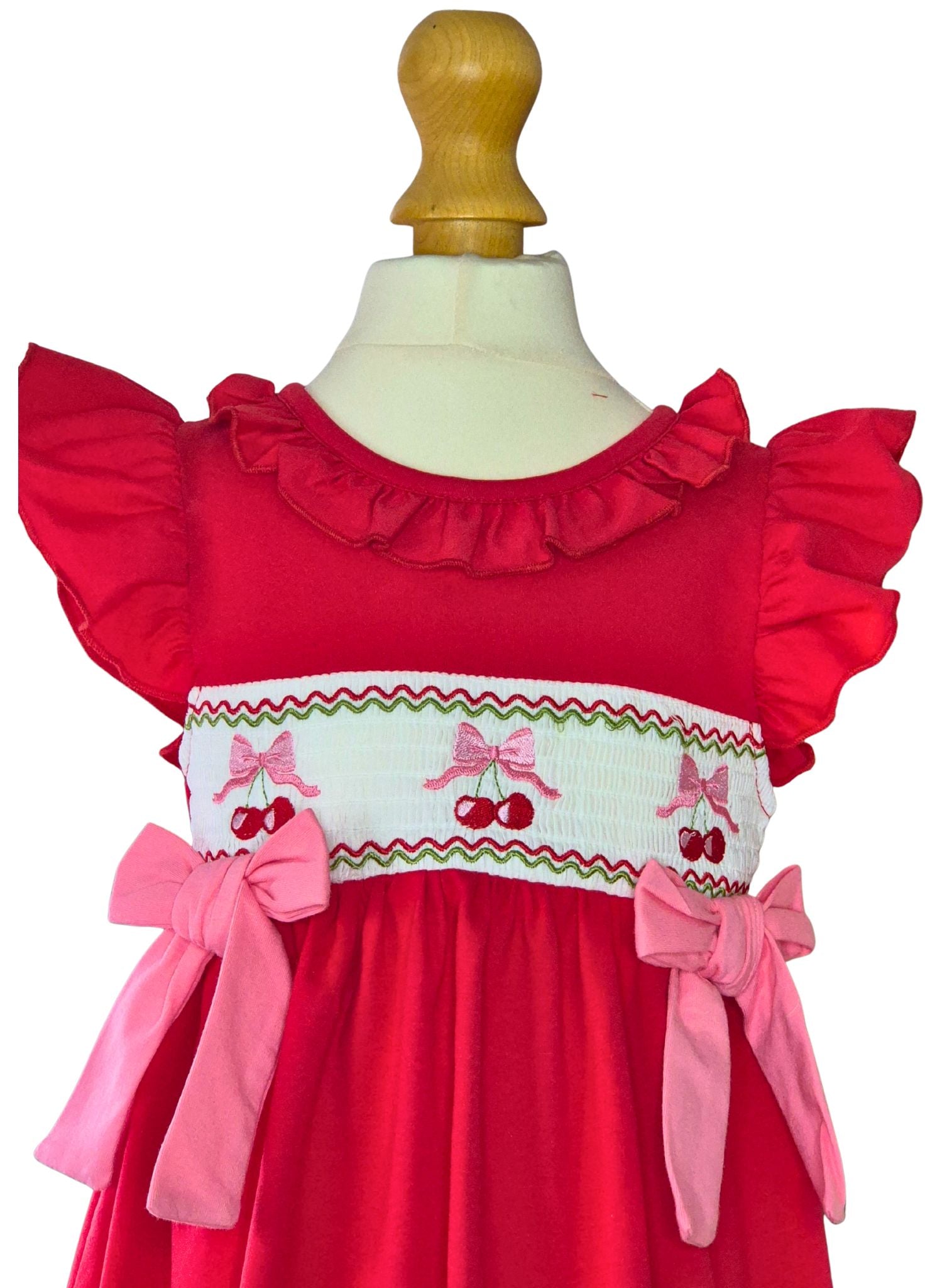 Red dress with ruffled sleeves and pink bows on a mannequin against a white background